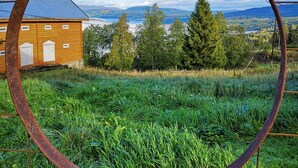 A rustic wooden building with a metal roof, surrounded by lush greenery and a clear blue sky. - Haugtun gårdspensjonat og kulturverksted (Nordre Land)