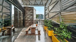 An outdoor terrace with a wooden bench, yellow planters, and a metal fence structure.