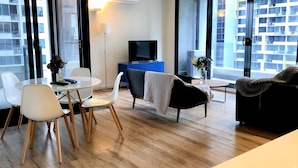 A modern living room with a dining area, a flat-screen TV, and large windows offering a city view.