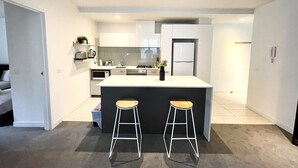 A modern kitchen with a central island, two bar stools, and white cabinetry.