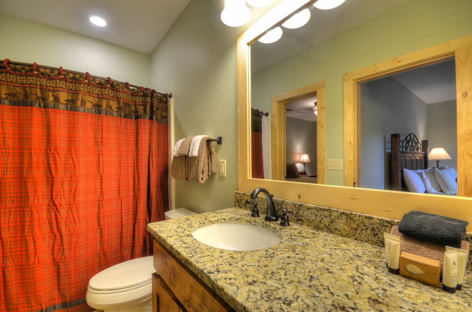 A bathroom with a granite countertop, a white sink, a mirror, and a red plaid shower curtain.