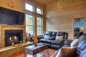 Ein gemütliches Blockhaus-Interieur mit Kamin aus Stein, Ledersofas und großen Fenstern.