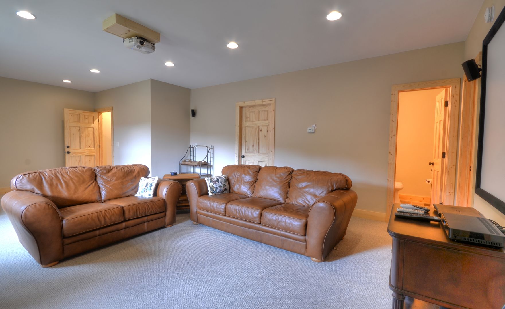 A living room with two brown leather sofas, a small wooden table, and a ceiling projector.