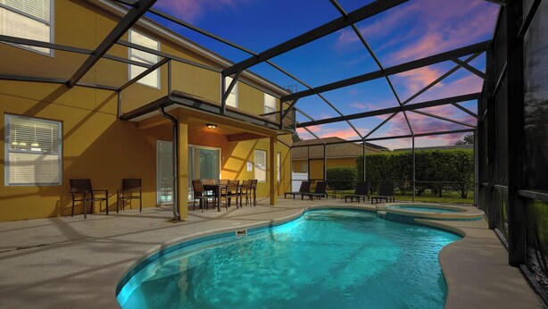Ein Schwimmbad mit Glasüberdachung, eine überdachte Terrasse mit Sitzgelegenheiten und ein Blick auf die umliegende Landschaft.