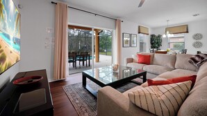 Ein modernes Wohnzimmer mit einem Glastisch, einem beigefarbenen Sofa und einem Essbereich mit Tisch und Stühlen.