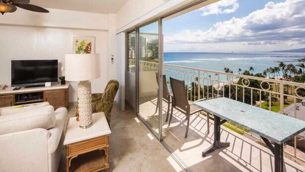 Un balcon avec vue sur l’océan, une télévision, une lampe et une table à manger.