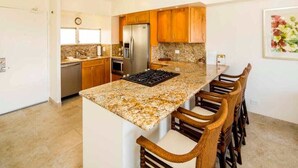 Une cuisine dotée de plans de travail en granit, d’armoires en bois, d’un réfrigérateur en acier inoxydable et d’une cuisinière à gaz encastrée.