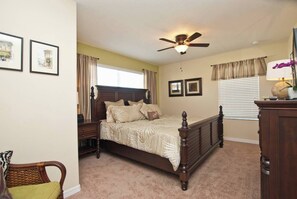 A bedroom with a bed, a ceiling fan, a window with curtains, and framed pictures on the wall.