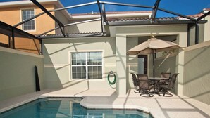 Una piscina con una zona prendisole, un tavolo e sedie, e un'area salotto coperta.