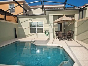 Una piscina con zona de patio, una mesa con sillas y un área de estar cubierta.