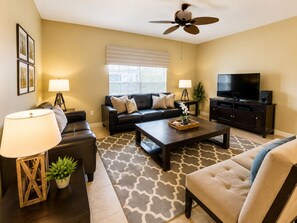 A living room with a sofa, coffee table, TV stand, and ceiling fan.