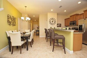 Una cocina con una isla central, armarios de madera, un reloj y un comedor con sillas y una mesa.