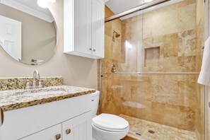 Ein Badezimmer mit Granitwaschtisch, Toilette in Weiß, einer Duschkabine aus Glas und einem weißen Schrank.