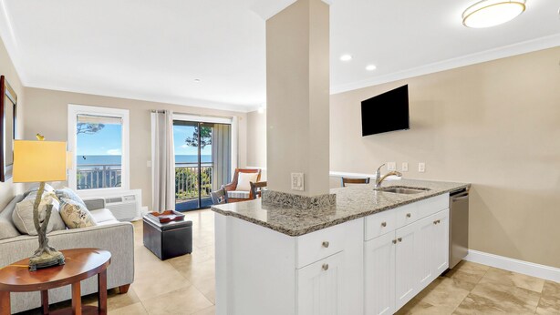 A modern kitchen with a central island, a dining area with a view, and a flat-screen TV mounted on the wall. - Stunning Oceanfront Villa! Oceanfront Pool (Hilton Head Island)