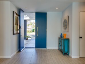 A hallway with a blue door, a framed picture on the left, a teal cabinet with orange items, and a door on the right.