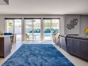 A modern living room with a grey sofa, a blue rug, and a pool view through glass doors.