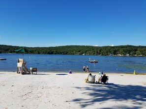 A beach with a lifeguard stand, clear blue water, and a forested hill in the background. - Mountain/lake community in Poconos,PA (Lackawaxen)