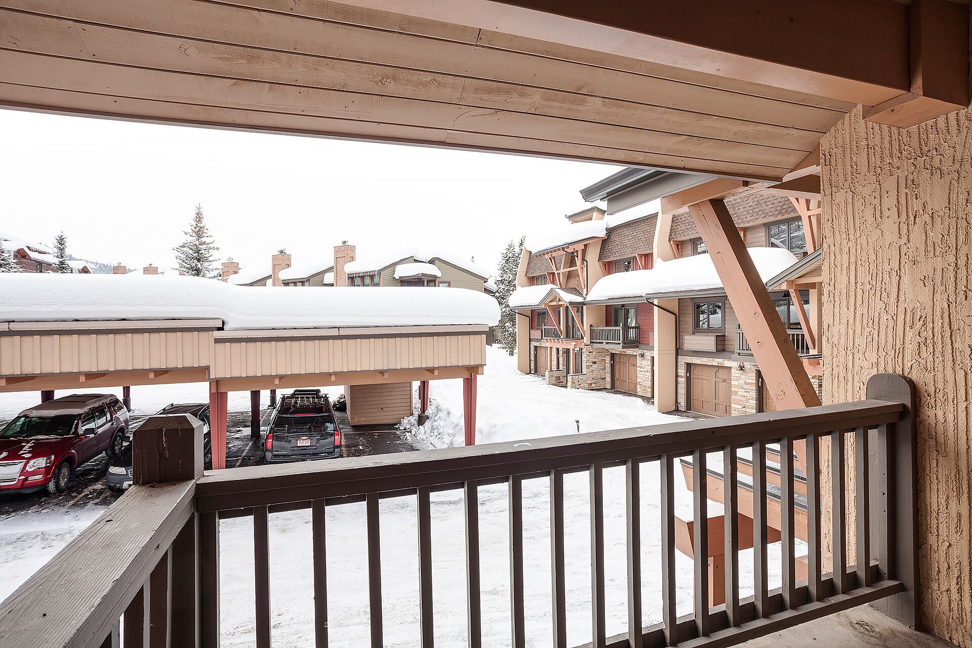 Un espacio exterior cubierto de nieve con una terraza de madera y vistas a edificios de varios pisos al fondo.
