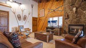 Ein rustikales Interieur mit Steinwand, Holzmöbeln, Kamin und aufgehängten Geweihen.