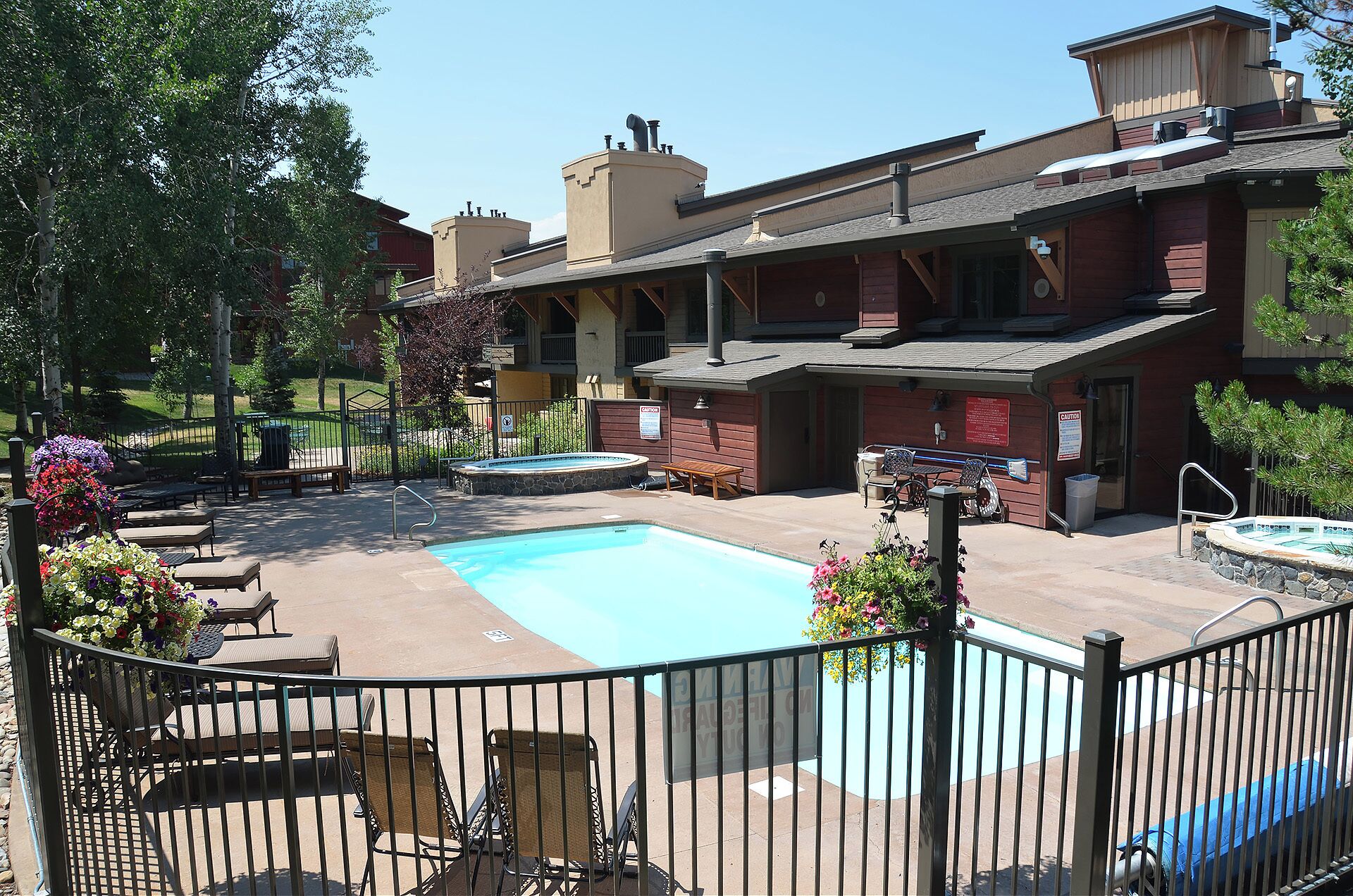 Un espace piscine doté de chaises longues et d’un jacuzzi, le tout entouré d’une clôture et bordé d’un bâtiment comportant plusieurs balcons.