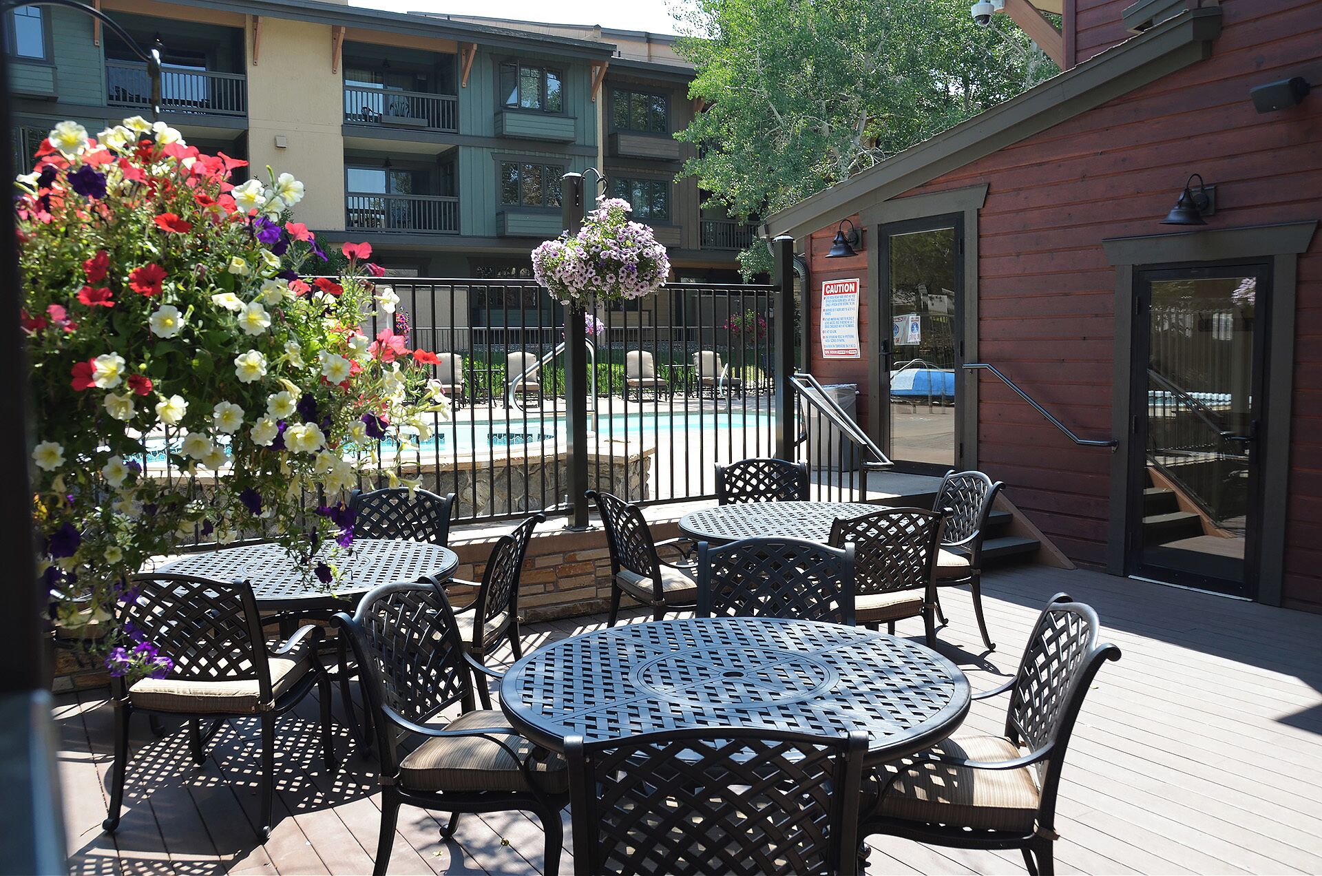 Une terrasse extérieure avec des tables et des chaises rondes, une piscine en arrière-plan et un bâtiment doté de balcons.