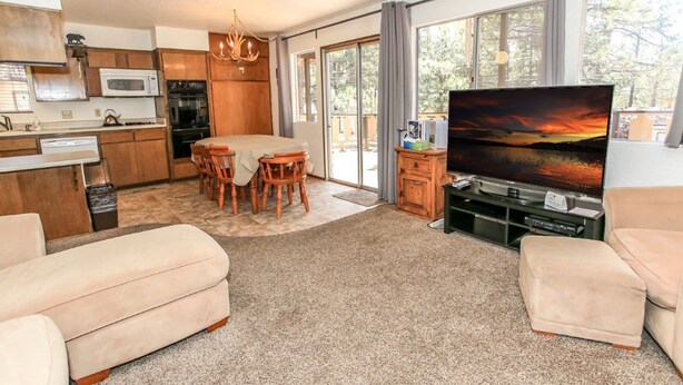A modern kitchen with wooden cabinets, a dining table, and a TV in the living area.