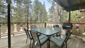 An outdoor patio with a glass-top table and chairs, surrounded by a wooden deck and a railing.