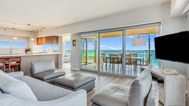 A modern living room with a large sofa, a flat-screen TV, and a view of the ocean through large sliding doors. - Luxe Life on the Ocean’s Edge w/Wraparound Lanai, Kitchen–Waikīkī Shore 500 (HONOLULU)