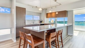 A modern kitchen with a large island, bar stools, and a view of the ocean. - Luxe Life on the Ocean’s Edge w/Wraparound Lanai, Kitchen–Waikīkī Shore 500 (HONOLULU)