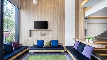 A modern living room with a wooden wall, a flat-screen TV, a bench with cushions, and a staircase.