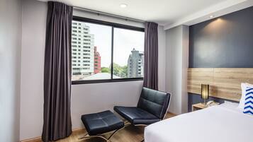 Una habitación de hotel con un ventanal grande, una cama, una silla y una mesita.