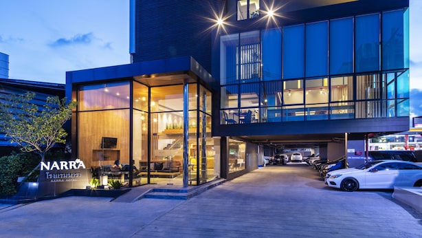 A modern hotel with a glass facade, outdoor seating area, and a parking garage. - Narra Hotel (Bangkok)