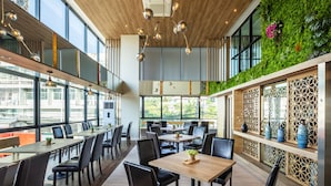 A modern restaurant with high ceilings, large windows, and a green wall with plants. Tables and chairs are arranged for dining. - Narra Hotel (Bangkok)