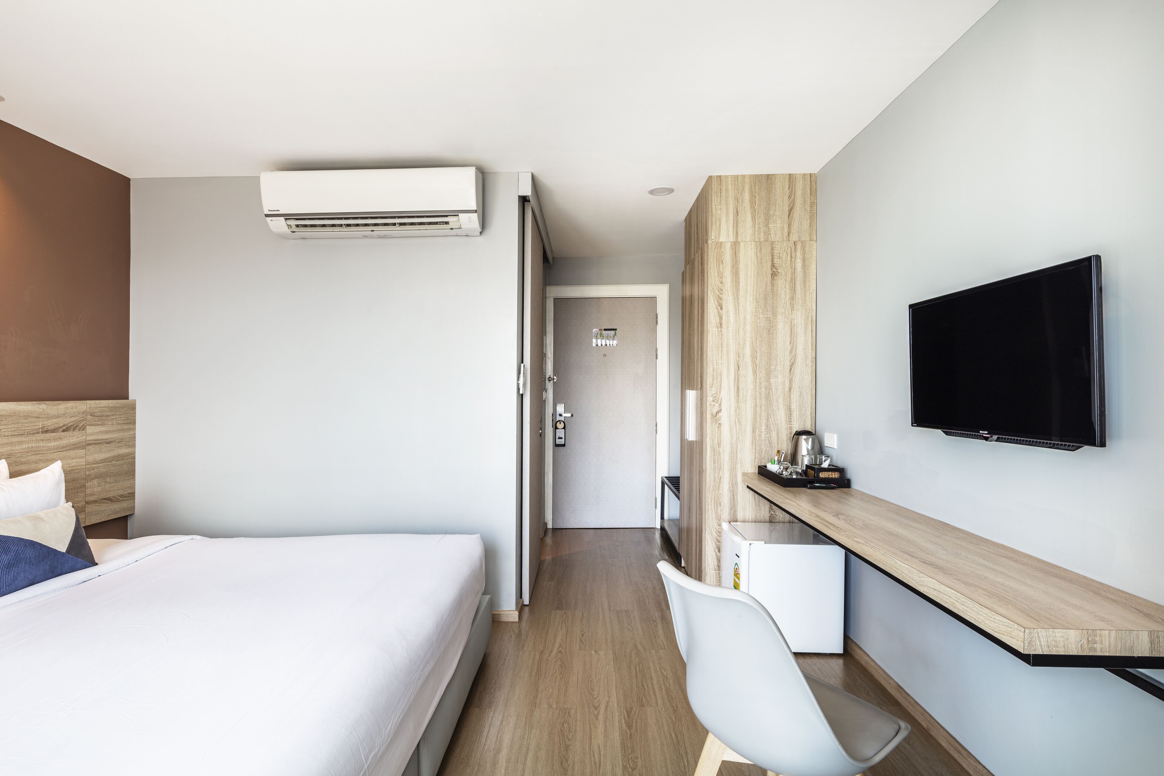 A hotel room with a bed, a desk, a chair, a television, and an air conditioning unit.
