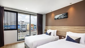 A hotel room with two beds, a large window with blinds, a city view, and a painting on the wall. - Narra Hotel (Bangkok)