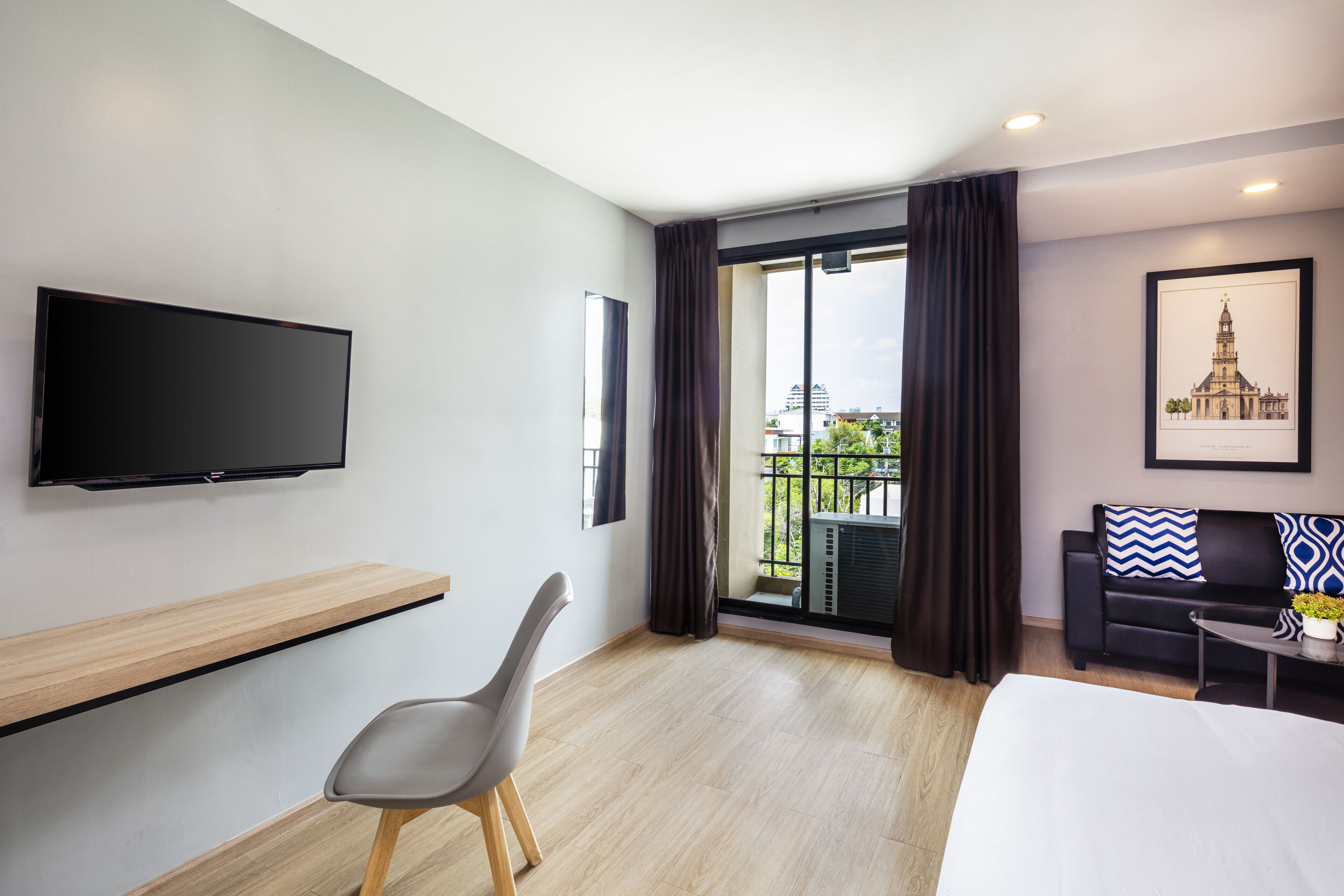 Une chambre d’hôtel comprenant un lit, un téléviseur fixé au mur, un bureau avec une chaise, un canapé et un balcon avec des rideaux.