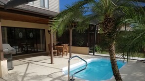 Una piscina con escalera metálica, rodeada de un patio con mesa y sillas, y una palmera.