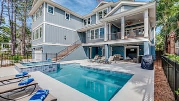 Una casa de dos pisos con piscina, mobiliario exterior y una escalera que sube al nivel superior.