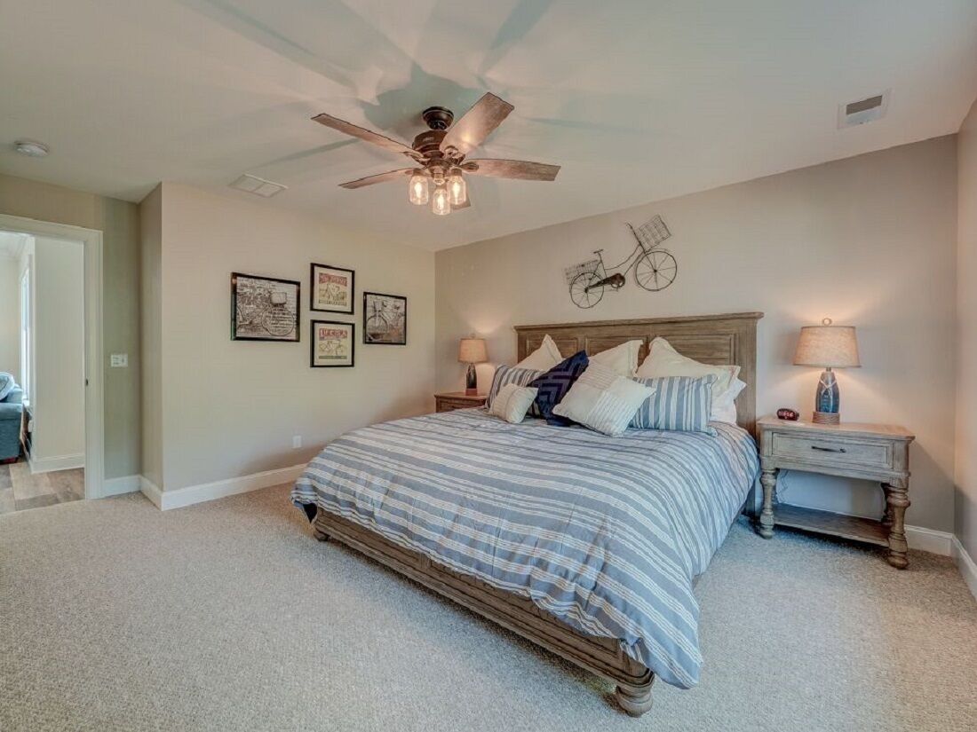 Une chambre à coucher comprenant un lit, deux tables de chevet, un ventilateur de plafond et des éléments de décoration murale.