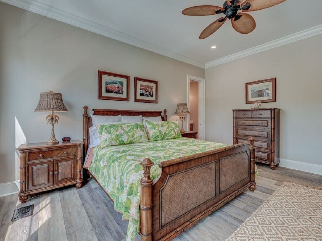 A bedroom with a wooden four-poster bed, a ceiling fan, and a wooden nightstand with a lamp.