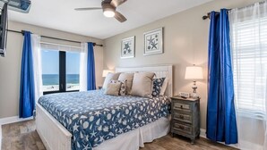 Un dormitorio con cama, mesita de noche, ventilador de techo y vista a la playa.