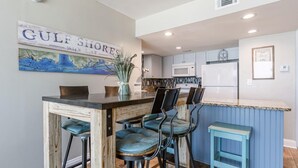Una cocina con zona de bar, que incluye una barra de madera, taburetes, un taburete azul y una isla de cocina con microondas y refrigerador.