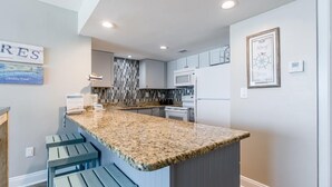 Una cocina moderna con encimera de granito, electrodomésticos integrados y una pequeña isla con taburetes de bar.