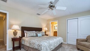 A bedroom with a bed, two bedside lamps, a ceiling fan, a door, and a chair. - Disney Escape | Private Pool | Resort Amenities | Sleeps 10 (Kissimmee)