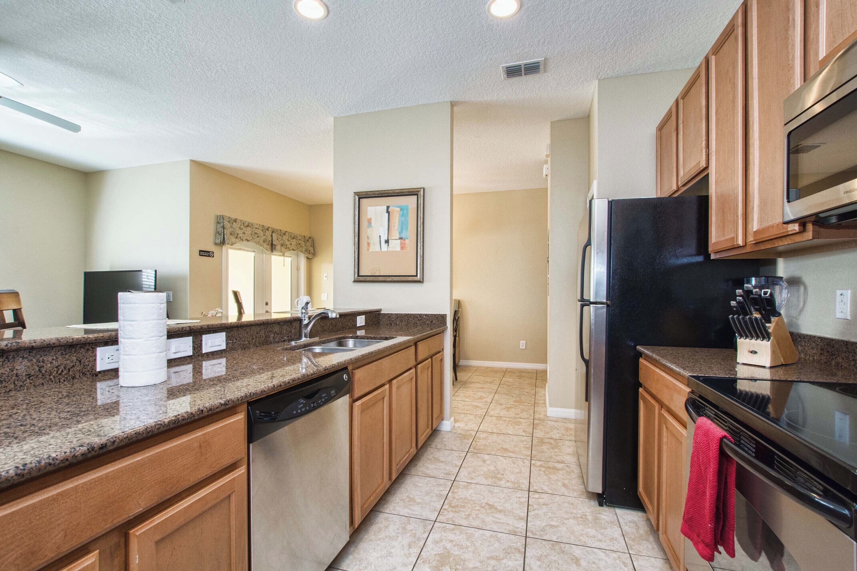 A kitchen with granite countertops, wooden cabinets, a stainless steel refrigerator, and a microwave.
