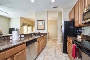 A kitchen with granite countertops, wooden cabinets, a stainless steel refrigerator, and a microwave. - Disney Escape | Private Pool | Resort Amenities | Sleeps 10 (Kissimmee)