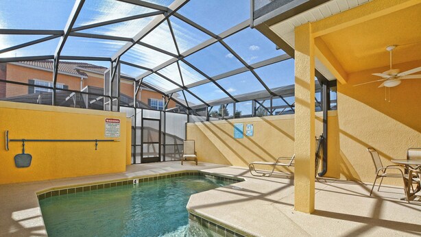 An indoor swimming pool with a glass ceiling, a pool safety sign, and a ceiling fan. - Disney Escape | Private Pool | Resort Amenities | Sleeps 10 (Kissimmee)