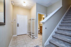 A hallway with a white door, a metal rack, and a staircase. - Disney Escape | Private Pool | Resort Amenities | Sleeps 10 (Kissimmee)