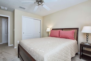 Une chambre à coucher avec un lit, deux lampes de chevet, un ventilateur de plafond et une porte.