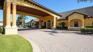 A yellow building with a covered entrance and a paved driveway. - Disney Escape | Private Pool | Resort Amenities | Sleeps 10 (Kissimmee)